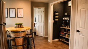 Une cuisine avec une table et des chaises en bois, un réfrigérateur et un coin café avec des étagères.