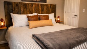 Un lit bien fait, avec une literie à rayures et un plaid marron, une tête de lit en bois et deux lampes de chevet.