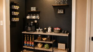 Un coin cuisine avec un espace dédié au café, des étagères remplies de tasses à café et un panneau indiquant : « Ce vin me donne des ailes. »