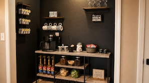Et tekøkken med kaffestation, reoler med kaffekopper og et skilt der siger 'Denne vin gør mig fantastisk'.