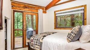 A bedroom with a bed, a window with a forest view, and a door leading outside. - A Hexagonal Cabin in the Trees, Two Miles From Alyeska (Girdwood)