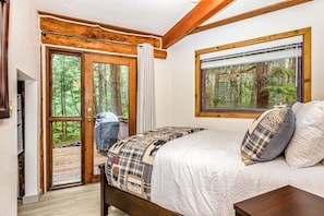 Ein Schlafzimmer mit Bett, einem Fenster mit Blick auf den Wald und einer Tür, die nach draußen führt.