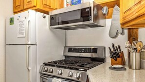 A kitchen with a white refrigerator, stainless steel stove, microwave, and wooden cabinets. - A Hexagonal Cabin in the Trees, Two Miles From Alyeska (Girdwood)