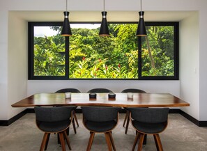 Une salle de conférence dotée d’une grande fenêtre donnant sur un jardin luxuriant, d’une table en bois et de quatre chaises.
