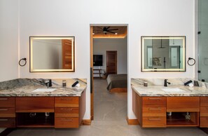 Um banheiro moderno com duas pias de mármore, armários de madeira e ventilador de teto.