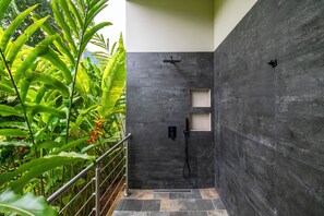 Área de chuveiro moderna com paredes de pedra escura, corrimão de metal e uma pequena prateleira.
