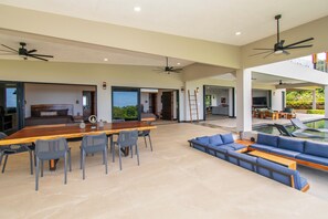 A spacious living area with a dining table, chairs, a sofa, and a pool. - Villa Serenity, 4-bedroom luxury ocean view with Pool and Trails Near Dominical (Uvita)