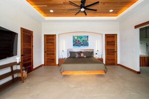 A bedroom with a bed centered in the room, flanked by wooden doors, a ceiling fan, and a painting above the bed. - Villa Serenity, 4-bedroom luxury ocean view with Pool and Trails Near Dominical (Uvita)