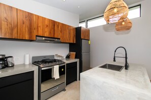 Eine moderne Küche mit Holzschränken, einem Edelstahlherd, einem Kühlschrank und einer Marmorarbeitsplatte.