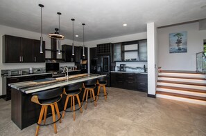 Une cuisine moderne avec des meubles de couleur sombre, un îlot central doté de tabourets de bar et un escalier dont les marches sont éclairées.