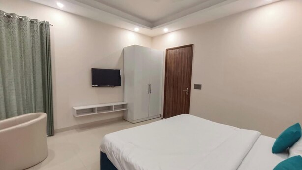 A bedroom with a bed, a wardrobe, a television, and a door. - Tipsyy Inn Suites 024 (Gurugram)
