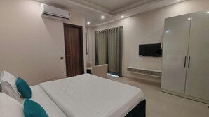 A hotel room with a bed, a wardrobe, a television, and a window with curtains. - Tipsyy Inn Suites 024 (Gurugram)