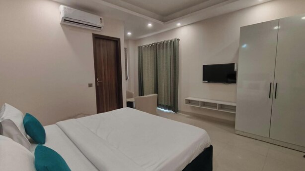 A hotel room with a bed, a wardrobe, a television, and a window with curtains. - Tipsyy Inn Suites 024 (Gurugram)