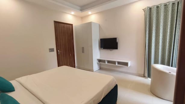 A bedroom with a bed, wardrobe, TV, and a small seating area. - Tipsyy Inn Suites 024 (Gurugram)