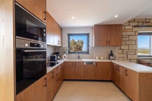 Eine moderne Küche mit Holzschränken, einem Bosch-Ofen, einer Kaffeemaschine und einer Steinwand.