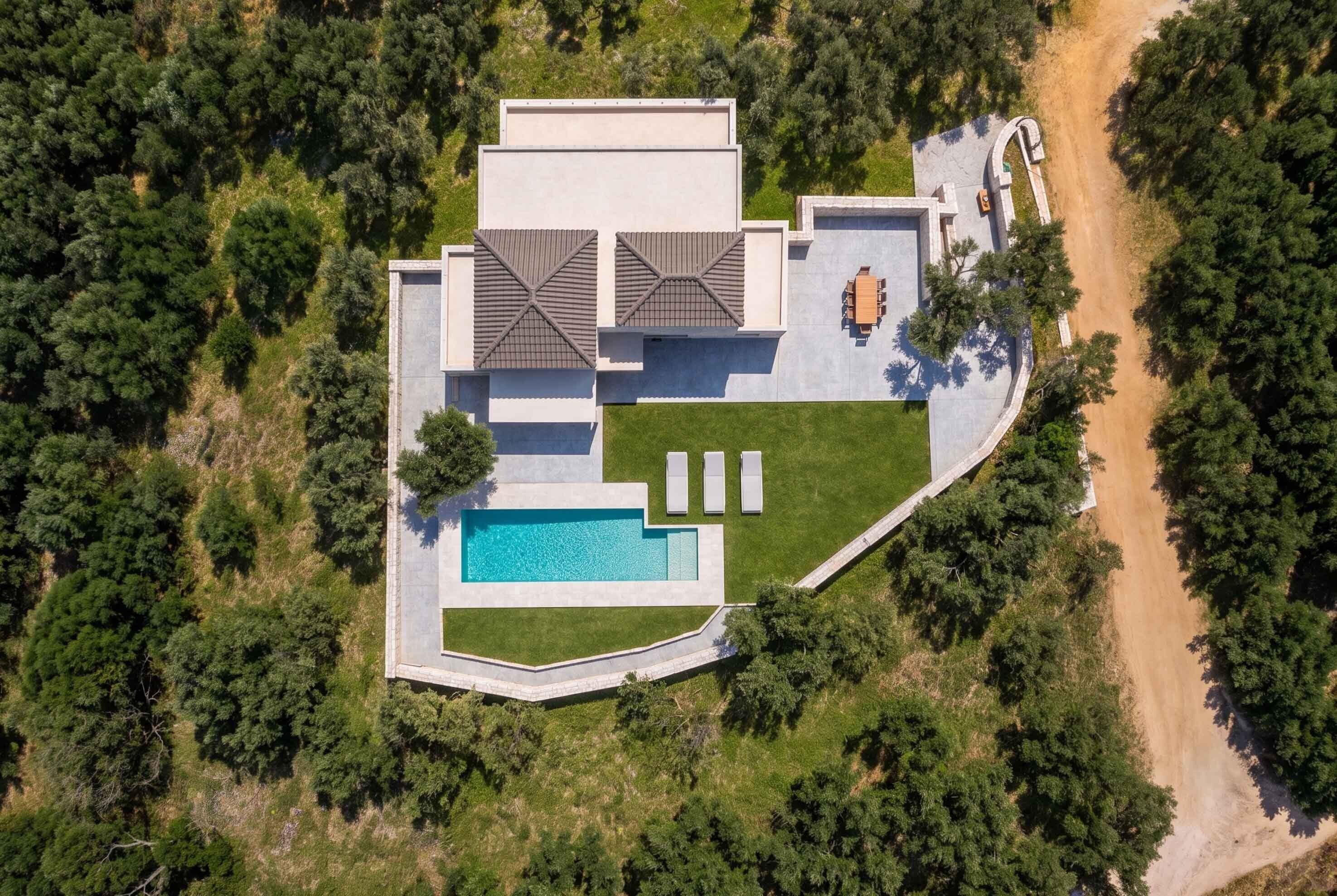 Una casa moderna con piscina, un patio amueblado y un camino de acceso.
