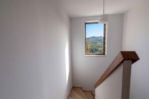 Gradi amb barana de fusta que condueix a una petita finestra amb vista a un paisatge amb pujols.