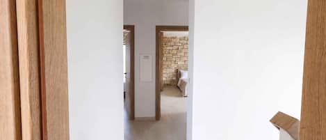 A hallway with a stone wall and a bed in the distance.