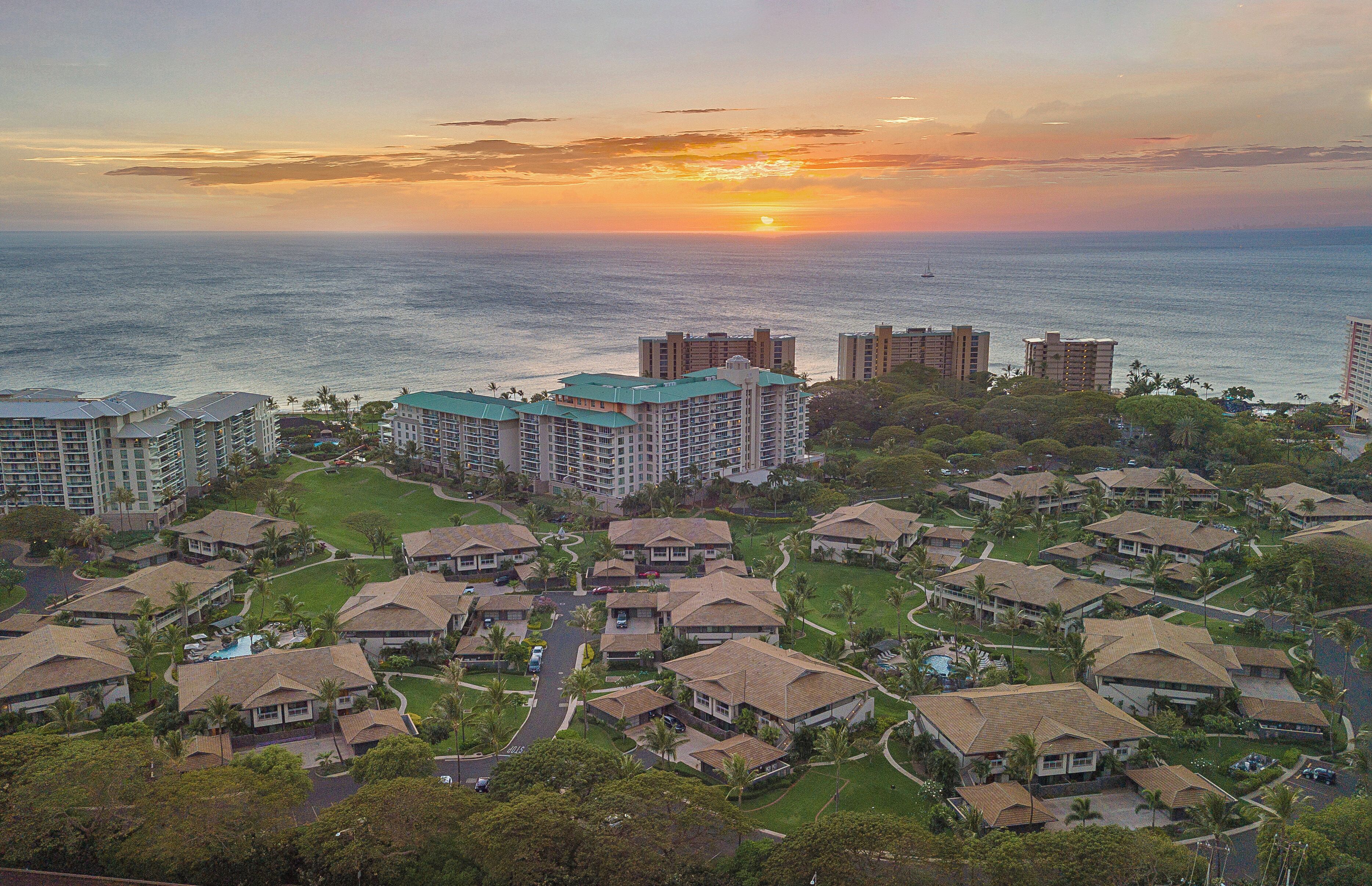 A resort with multiple buildings, a swimming pool, and a view of the ocean at sunset.