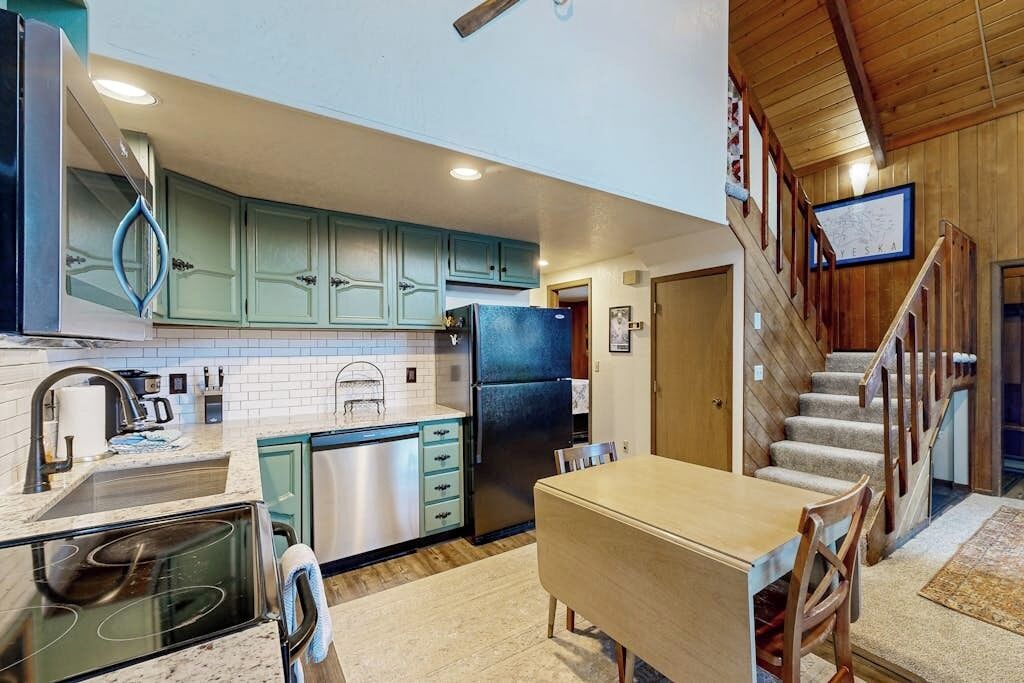 A kitchen with teal cabinets, a stainless steel refrigerator, and a dining area with a wooden table and chairs.