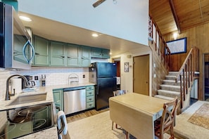 A kitchen with teal cabinets, a stainless steel refrigerator, and a dining area with a wooden table and chairs. - Classic Alyeska A-frame From the Resort's Early Days (Girdwood)