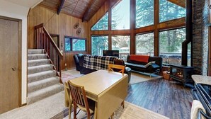 A spacious living area with a fireplace, a sofa, a dining table, and a staircase leading to another level. - Classic Alyeska A-frame From the Resort's Early Days (Girdwood)