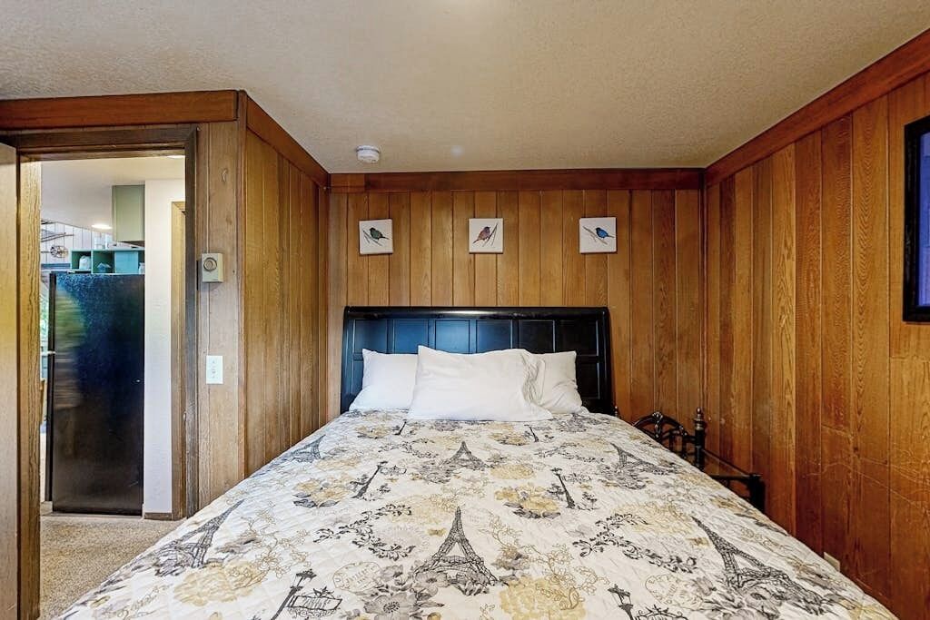 A bedroom with a wooden headboard, a bed with a patterned bedspread, and three wall-mounted pictures.