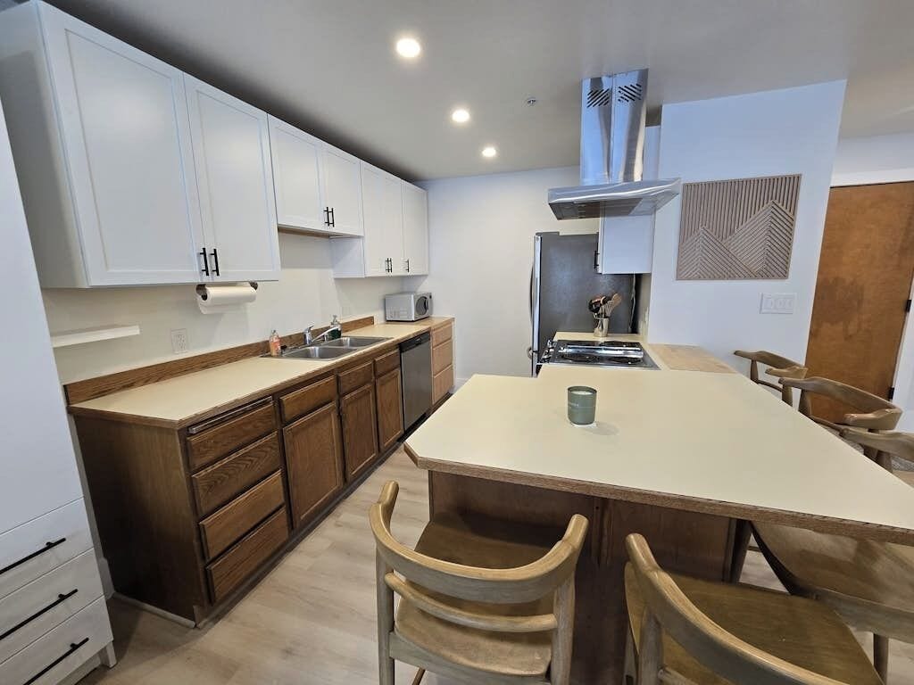 A modern kitchen with white cabinets, a central island, and wooden chairs.