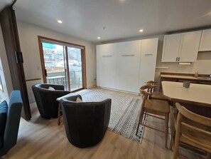 Cocina moderna con armarios blancos, comedor con mesa y sillas, y un amplio ventanal corredizo que da a un balcón.