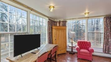 Una habitación con un ventanal grande, un televisor, una mesa de madera, un sillón rojo y un armario.