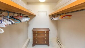 Um closet pequeno com prateleiras de madeira em ambos os lados, uma cômoda central e uma luminária no teto.