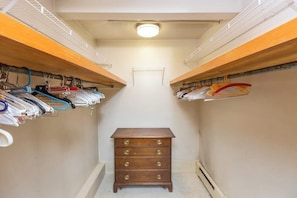 A narrow walk-in closet with wooden shelving on both sides, a central dresser, and a ceiling light.