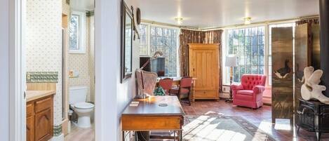 A room with a wooden desk, a red chair, a fireplace, and a large window.