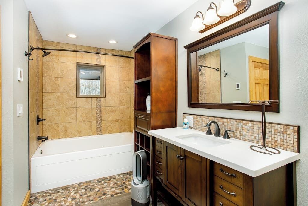 A modern bathroom with a bathtub, a large mirror, and a vanity with a sink.