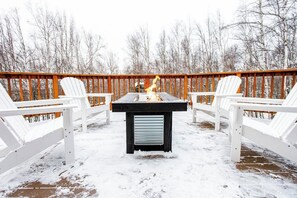 A deck with a table and chairs, surrounded by a wooden railing, set against a snowy landscape. - Birch Forest Cabin Retreat W/hot Tub & Anchorage (Chugiak)