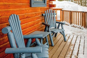 Een houten terras met twee Adirondack-stoelen en een houten tafel.