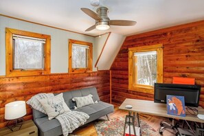 A cozy cabin interior with a sofa, a desk, and a television. - Birch Forest Cabin Retreat W/hot Tub & Anchorage (Chugiak)