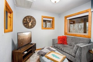 A living room with a television, a clock, a window, and a sofa. - Birch Forest Cabin Retreat W/hot Tub & Anchorage (Chugiak)