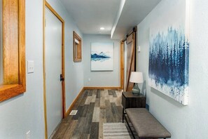 A hallway with wooden doors, a bench, a lamp, and a painting on the wall. - Birch Forest Cabin Retreat W/hot Tub & Anchorage (Chugiak)