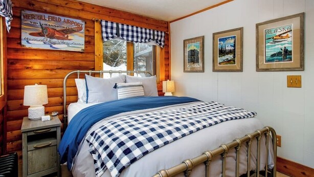 Una camera da letto con un letto, un comodino, una lampada, una coperta a quadri e quadri appesi al muro.