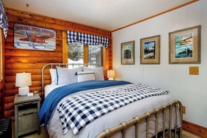 Une chambre avec un lit, une table de chevet, une lampe, une couverture à carreaux et des tableaux encadrés accrochés au mur.