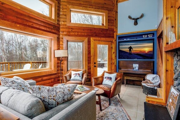 L’intérieur d’une cabane en rondins, avec un canapé, des fauteuils, un téléviseur et une cheminée.