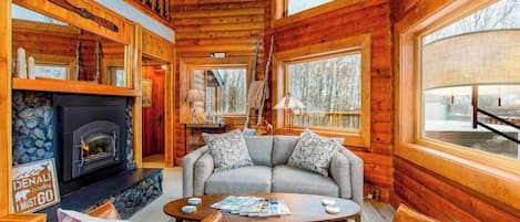 A cozy cabin interior with a stone fireplace, a gray sofa, and a wooden ceiling.