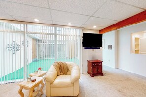 A room with a sliding glass door leading to a balcony, a leather armchair, a small wooden table, and a television mounted on the wall. - Anchorage Flat Between Bootlegger Cove & Downtown (Anchorage)