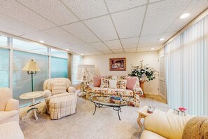 A spacious living room with a large window, a floral sofa, a striped armchair, and a coffee table. - Anchorage Flat Between Bootlegger Cove & Downtown (Anchorage)