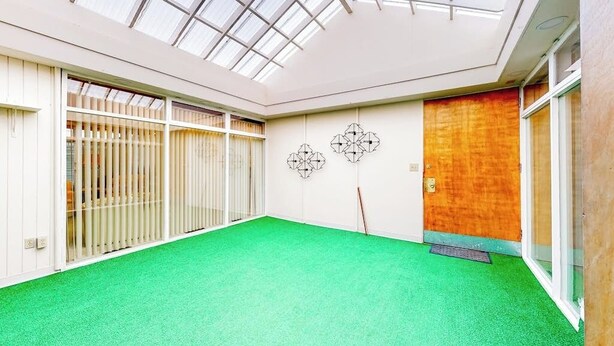 Una habitación con alfombra verde, puerta de madera y tragaluz.