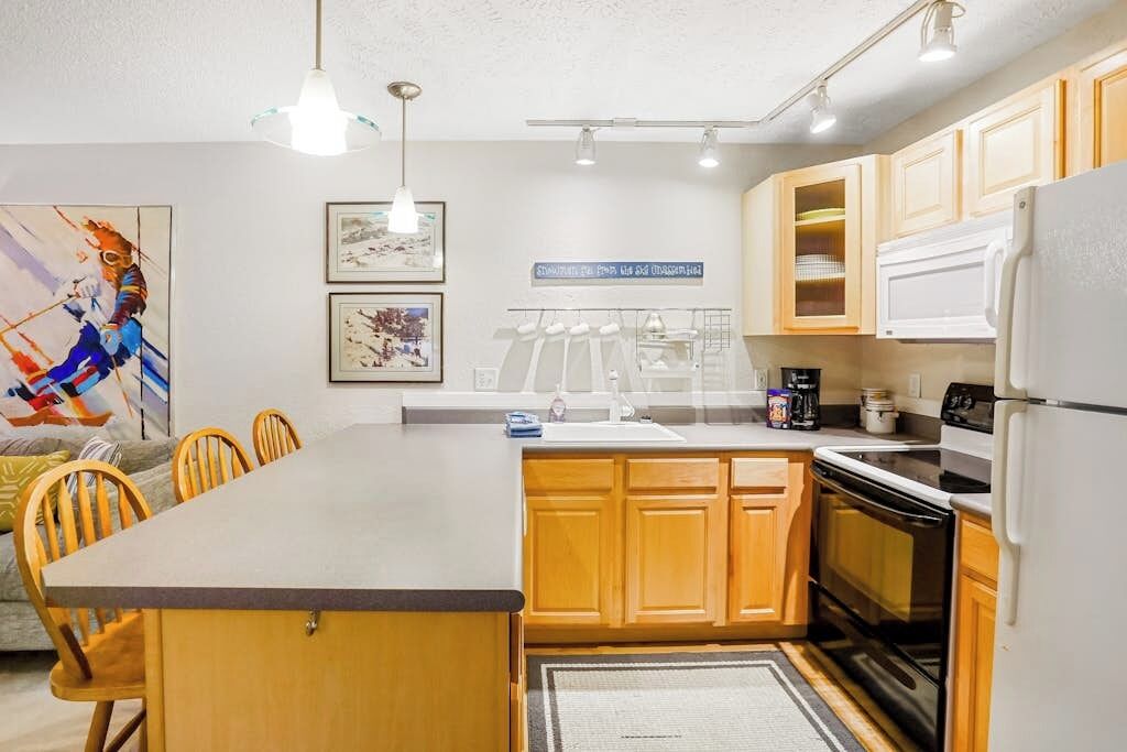 A modern kitchen with wooden cabinets, a central island, and a dining area with chairs.