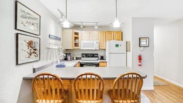 A kitchen with wooden cabinets, a white refrigerator, a microwave, and a stove. There are three wooden chairs at the island.