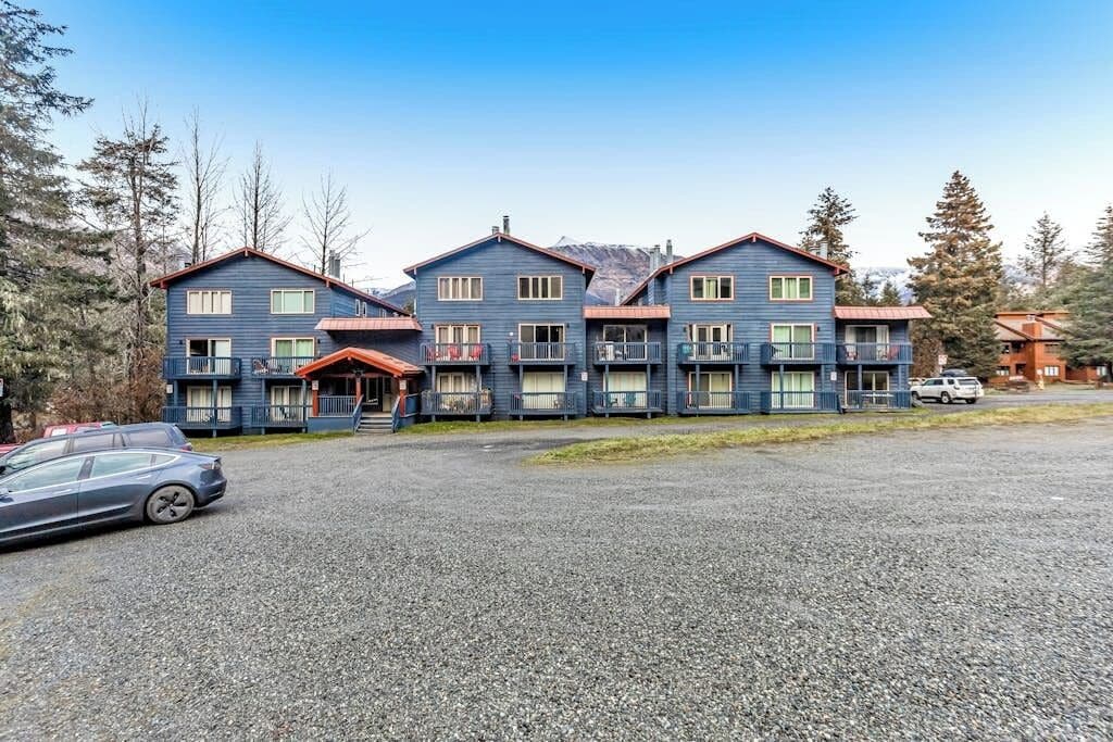 A multi-story building with a gravel driveway and parked cars.
