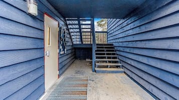 A narrow hallway with a metal grate floor, a wooden door, and a staircase leading to an upper level.